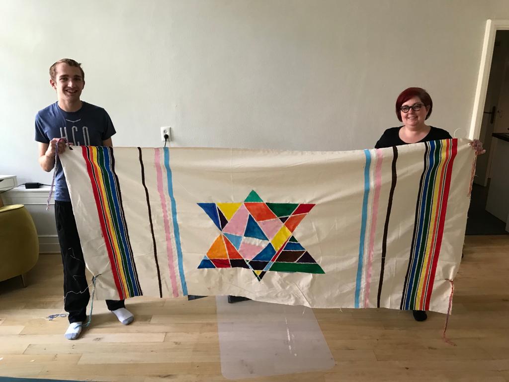 The Oy Vey Pride banner: Rainbow stripes like on a tallit (tallis) with a multi-colored magen david in the middle.