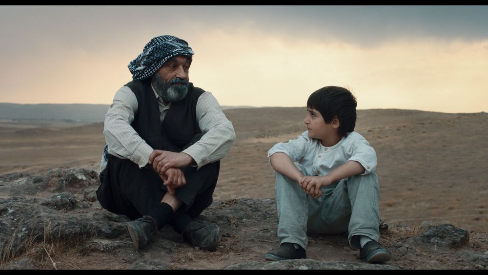 Man en kind staren elkaar zitten naast elkaar aan in de woestijn in film Neighbours van Mano Khalil